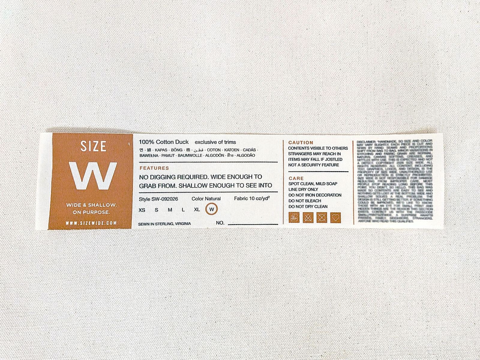 The SIZE WIDE garment label laid on canvas, reading wide and shallow, on purpose.