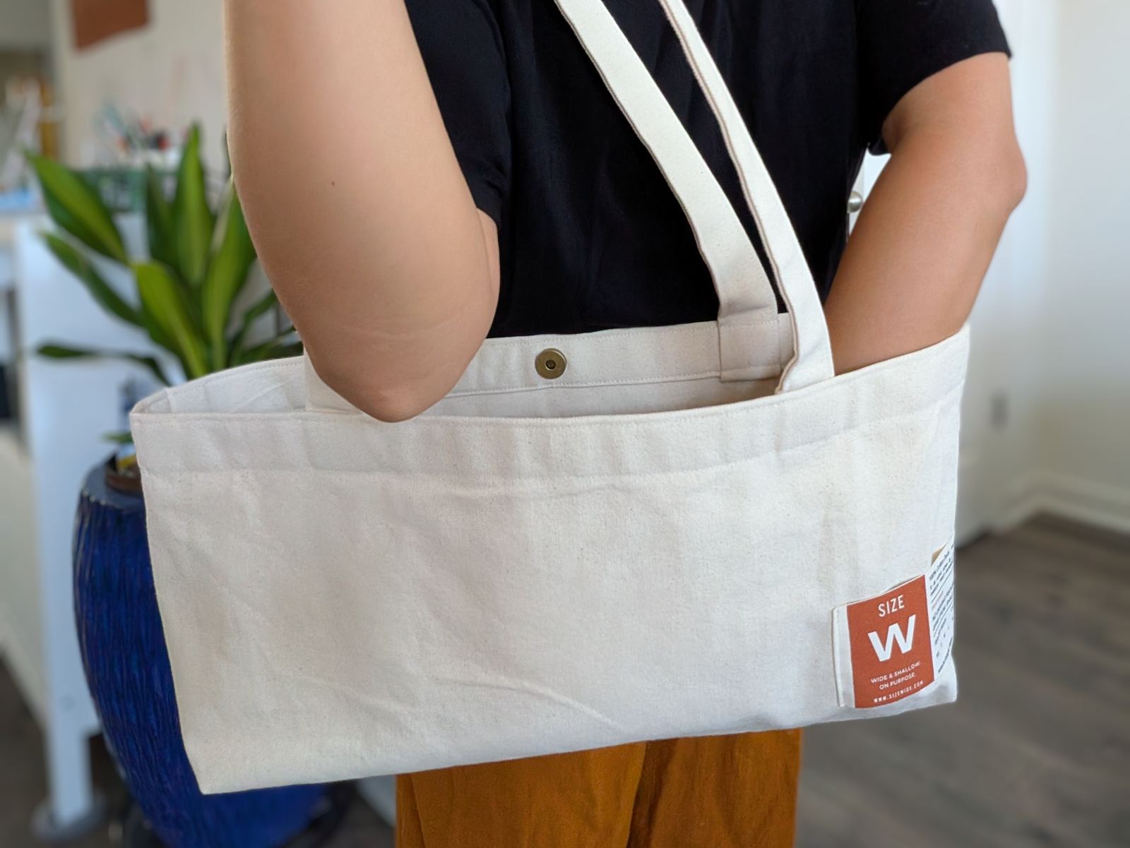 Close view of the tote on the shoulder, with the brass snap closure and the rust SIZE W label.