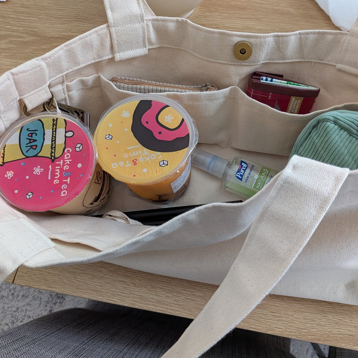 Looking down into the tote on a table: two sealed boba teas standing upright, with a pouch and wallet in the inner pockets.