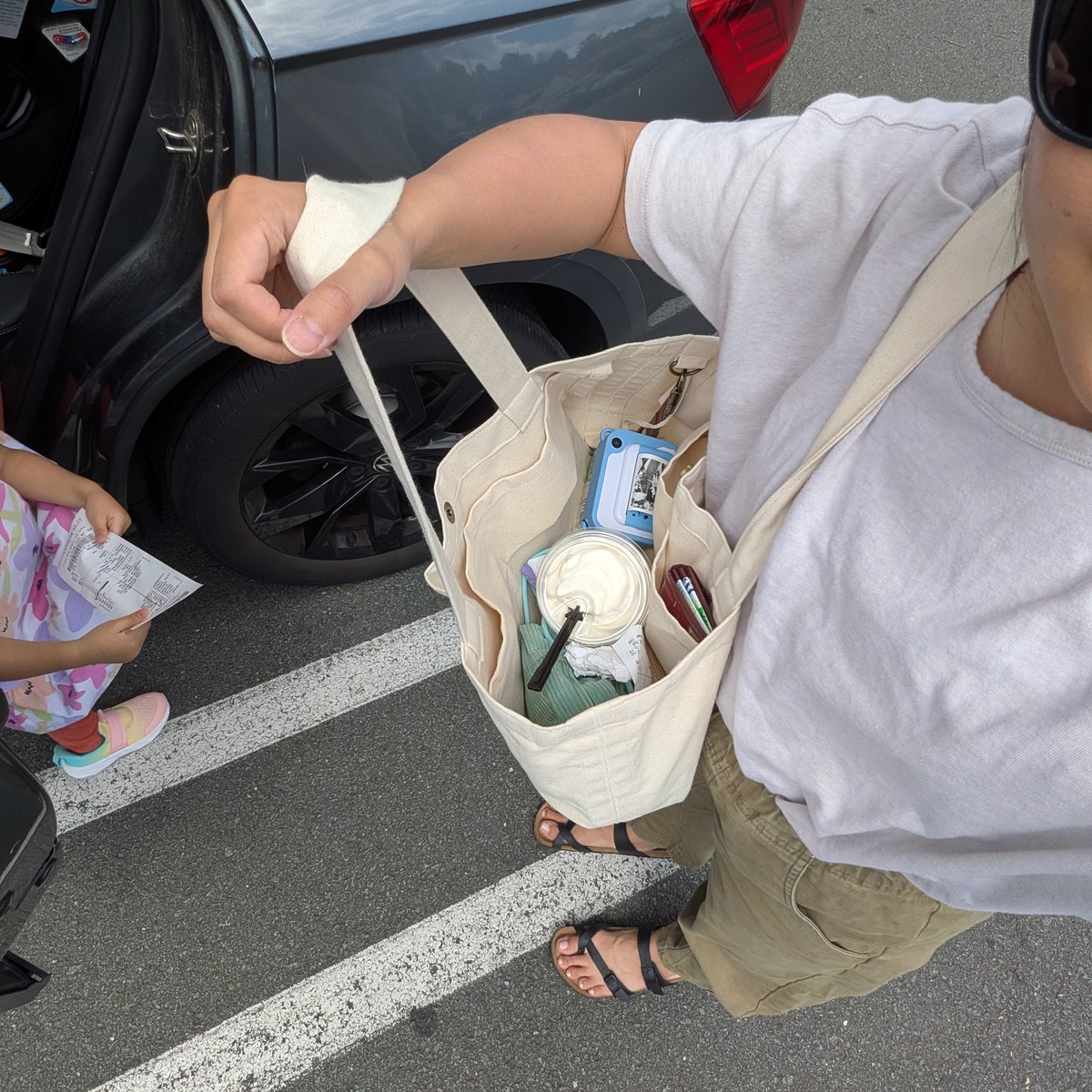 The tote carried on the shoulder in a parking lot, with a Costco vanilla cup sitting flat inside next to a tablet.